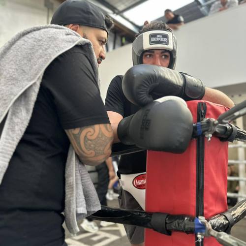 A coach working a boxer in headgear through rounds in the corner of the ring